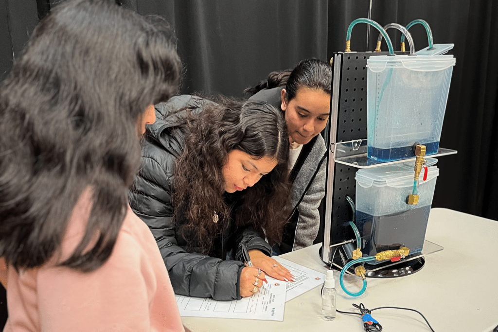 Students engaging in hands-on career exploration activity at BridgeYear's Career Test Drive® Fair, observing a water filtration setup and documenting their findings.