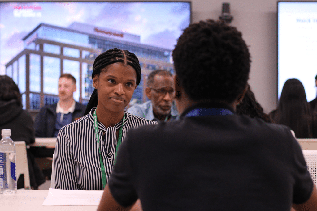 Young woman engaged in career counseling conversation during BridgeYear's Career Test Drive® Fair, with diverse participants in background and corporate setting.