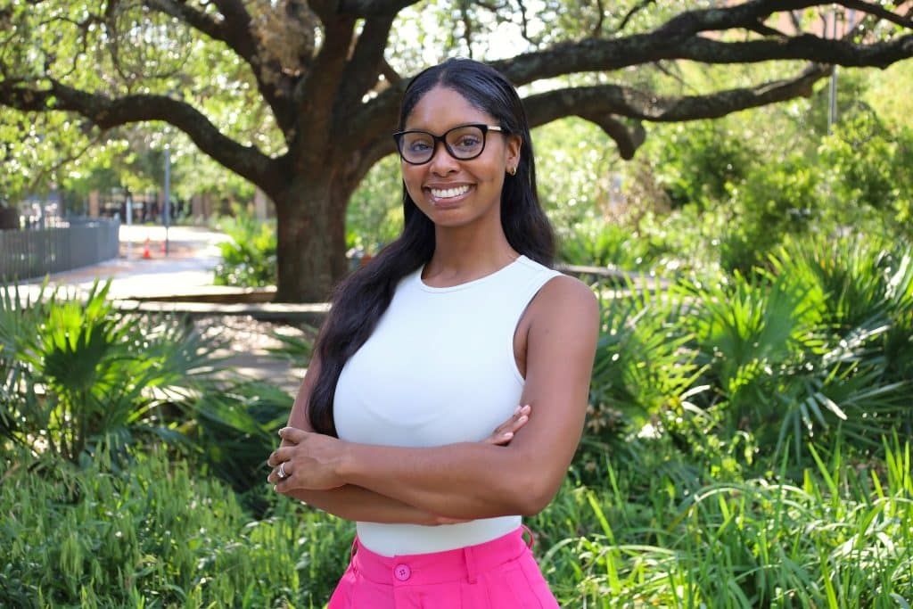 Imani Raglin, Operations Manager at BridgeYear, smiling outdoors with greenery and a large tree in the background, representing the organization's commitment to supporting students from underserved communities.