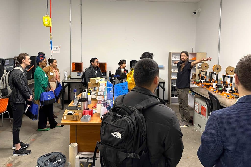 Participants engaged in a guided tour at TXRX Labs, observing 3D printers and innovative resources, while an instructor explains opportunities for skill development.