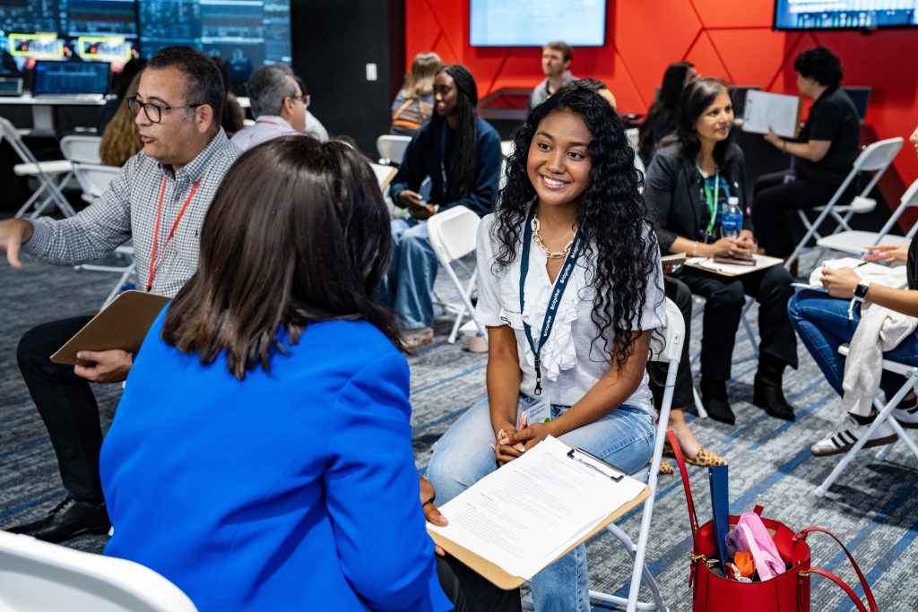 Students engaging in career exploration discussions during BridgeYear's program, featuring a young woman smiling while seated with a clipboard, surrounded by peers and professionals in a collaborative environment.