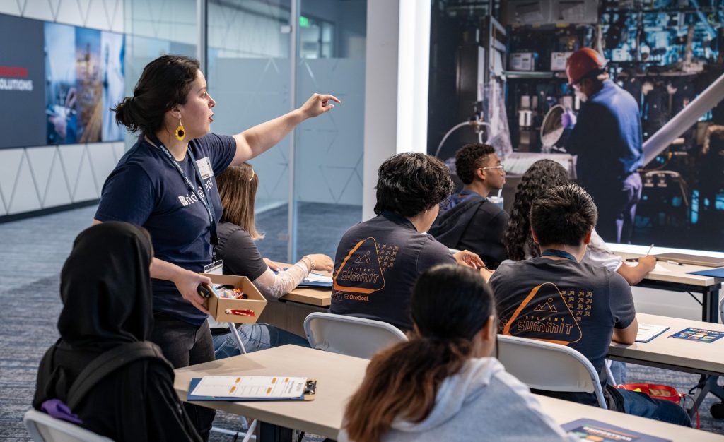 Instructor engaging students at BridgeYear's Essential Soft Skills for Success Conference, with participants in professional attire focused on learning, and a backdrop featuring industrial work setting.